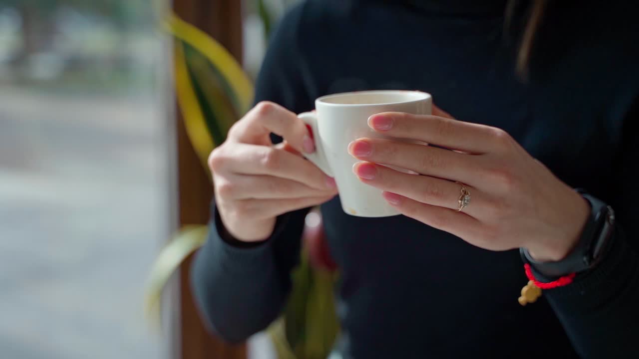 White cup with coffee in woman's hands. Beautiful young woman enjoying hot drink in a cafe. Slow motion.