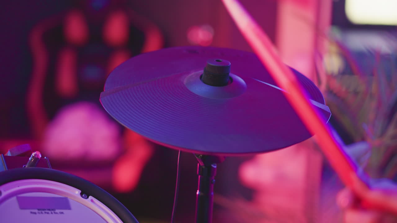 Close up of electronic cymbal being hit by drummer with red stick in vibrant studio filled with magenta and purple lights capturing sound dynamics and musical action in energetic performance setting