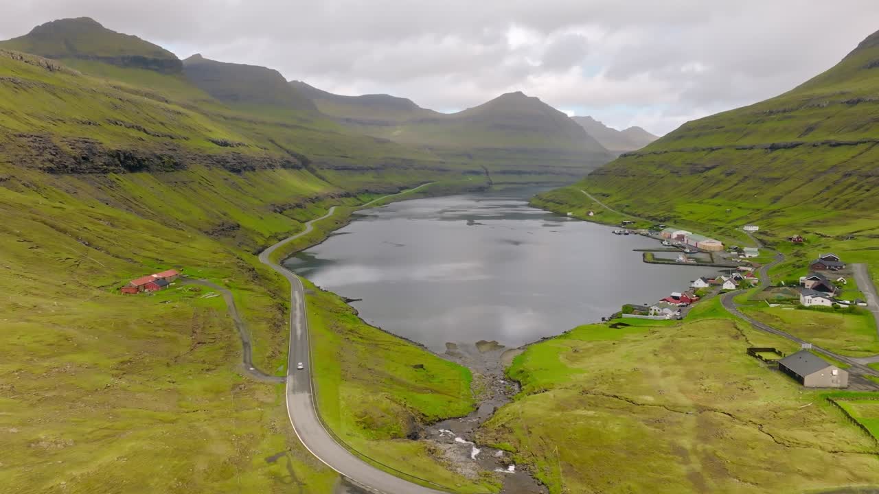 A scenic valley with green hills, a serene lake, small village houses, and winding roads