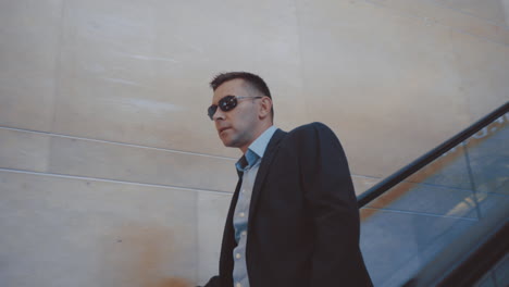 Modern-man-in-stylish-suit-and-sunglasses-going-down-on-escalator