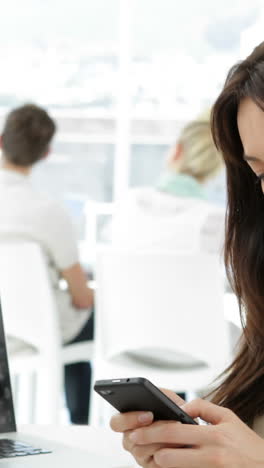 mujer trabajando en su escritorio enviando mensajes de texto por teléfono