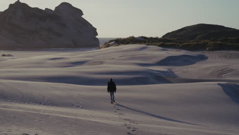 person walking through sand dunes at the beach