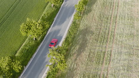 telephoto aerial following a classic muscle car driving on a sunlit asphalt road