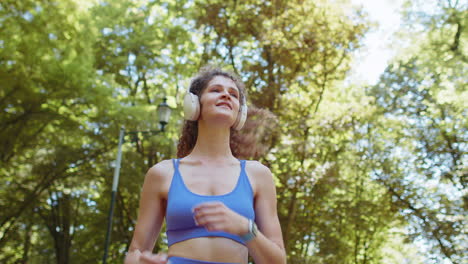 aktive fitness-joggerin frau läuft, trainiert, läuft marathon, hört musik in drahtlosen kopfhörern im park