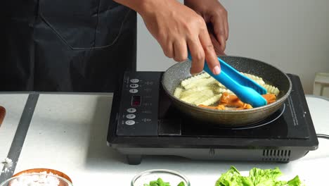person frying french fries and sausages on an induction cooker