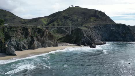 Drohne-Fliegt-über-Das-Wasser-Und-Zeigt-Einen-Wunderschönen-Strand-Unter-Einer-Der-Berühmten-Brücken-Entlang-Des-Highway-101-In-Der-Nähe-Von-Big-Sur,-Kalifornien