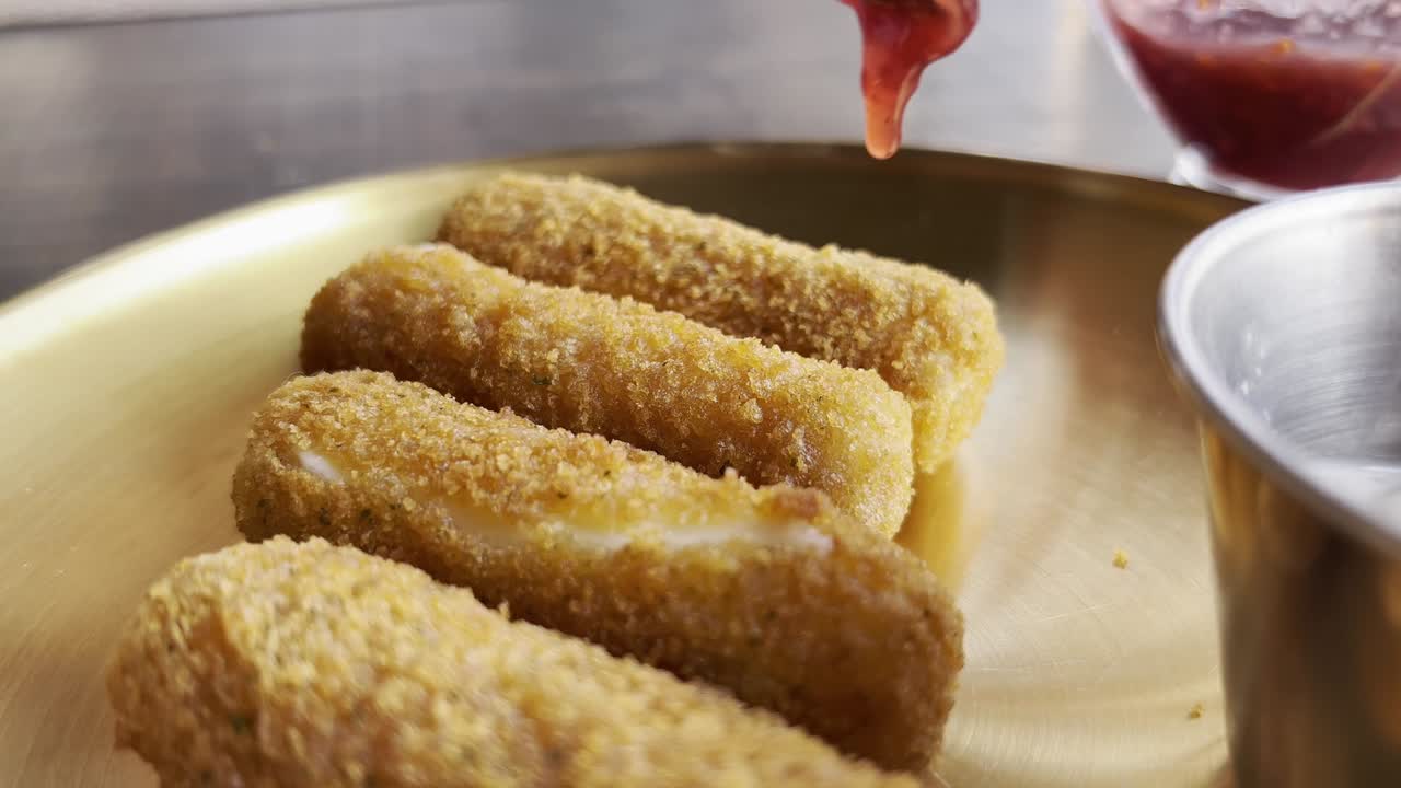 Golden-brown mozzarella sticks served on a brass plate with a side of dipping sauce in a casual dining setting