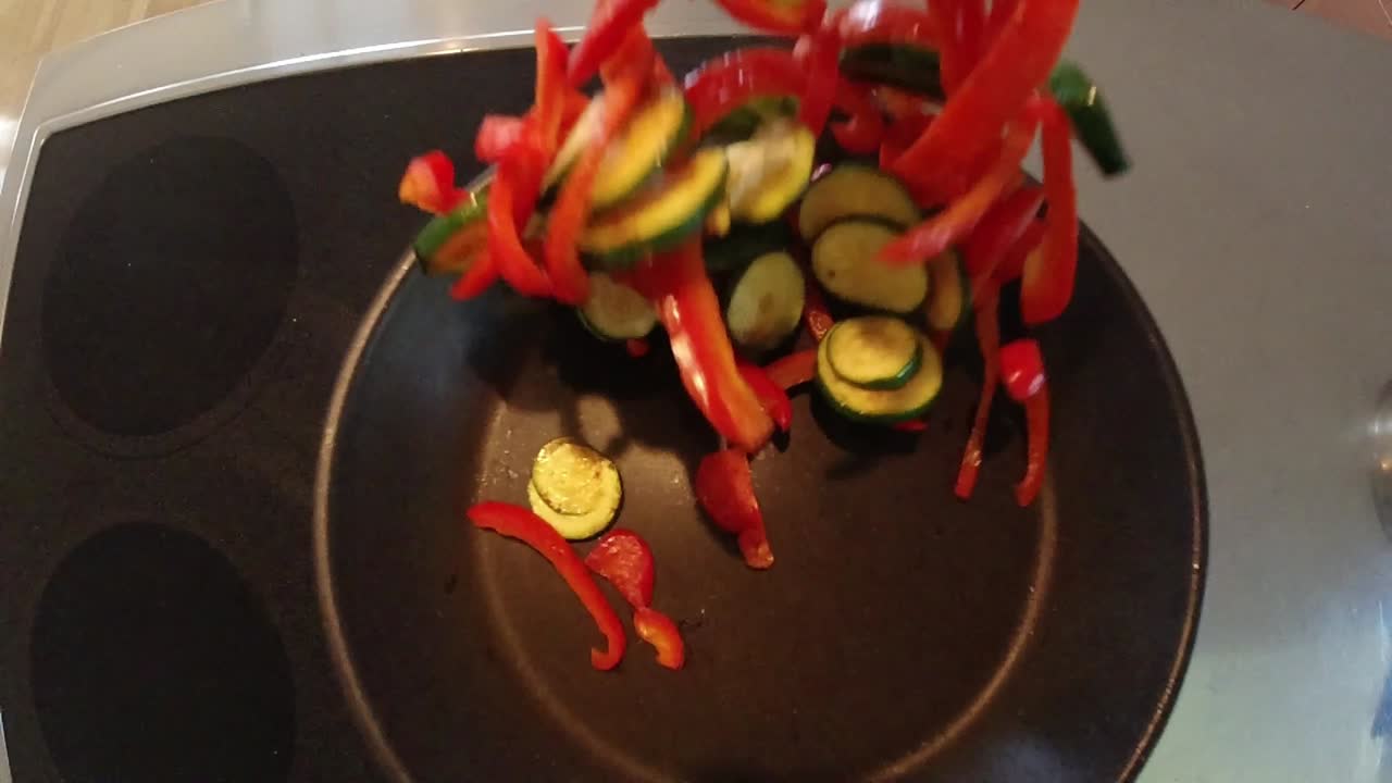 Slow-motion video of a chef stirring and mixing vegetables in a frying pan with oil in a non-commercial kitchen.