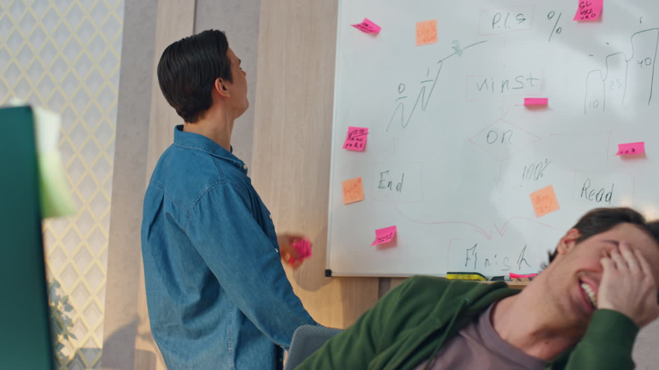 우스스러운 남자가 표지판을 붙이고 장난하는 캐비. 동료들이 함께 웃고