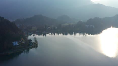 Vista-Aérea-Matutina-Sobre-El-Lago-Bled-Con-El-Reflejo-Del-Sol-En-La-Superficie-Del-Lago