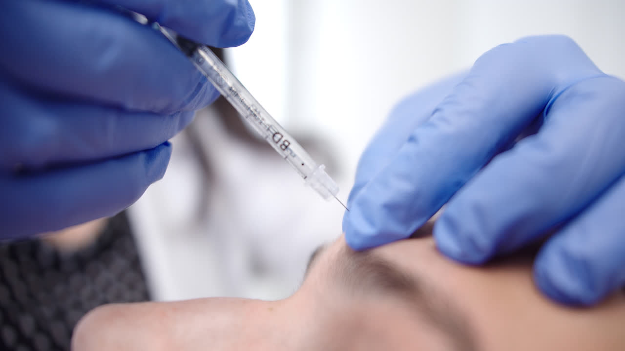 Beautiful super close-up shot of a patient being injected with cosmetic medicine in a dermatology clinic by a female doctor wearing blue gloves.