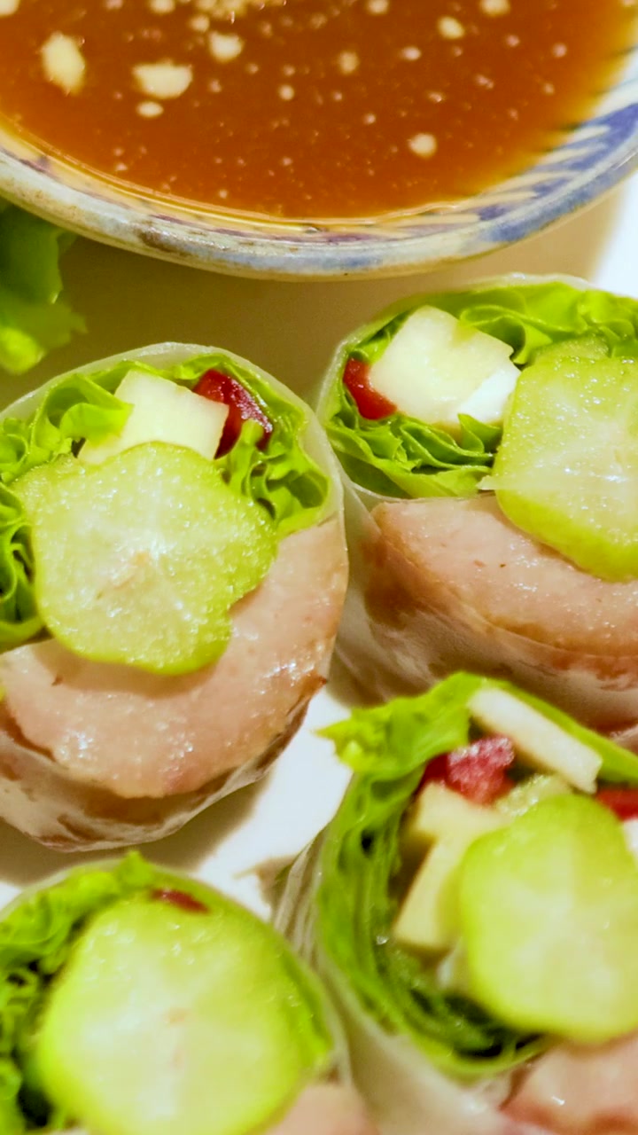 Close-up lumpia babi Vietnam dan saus cocol, menyoroti bahan-bahan segar dan warna-warna cerah dalam suasana yang terang benderang.