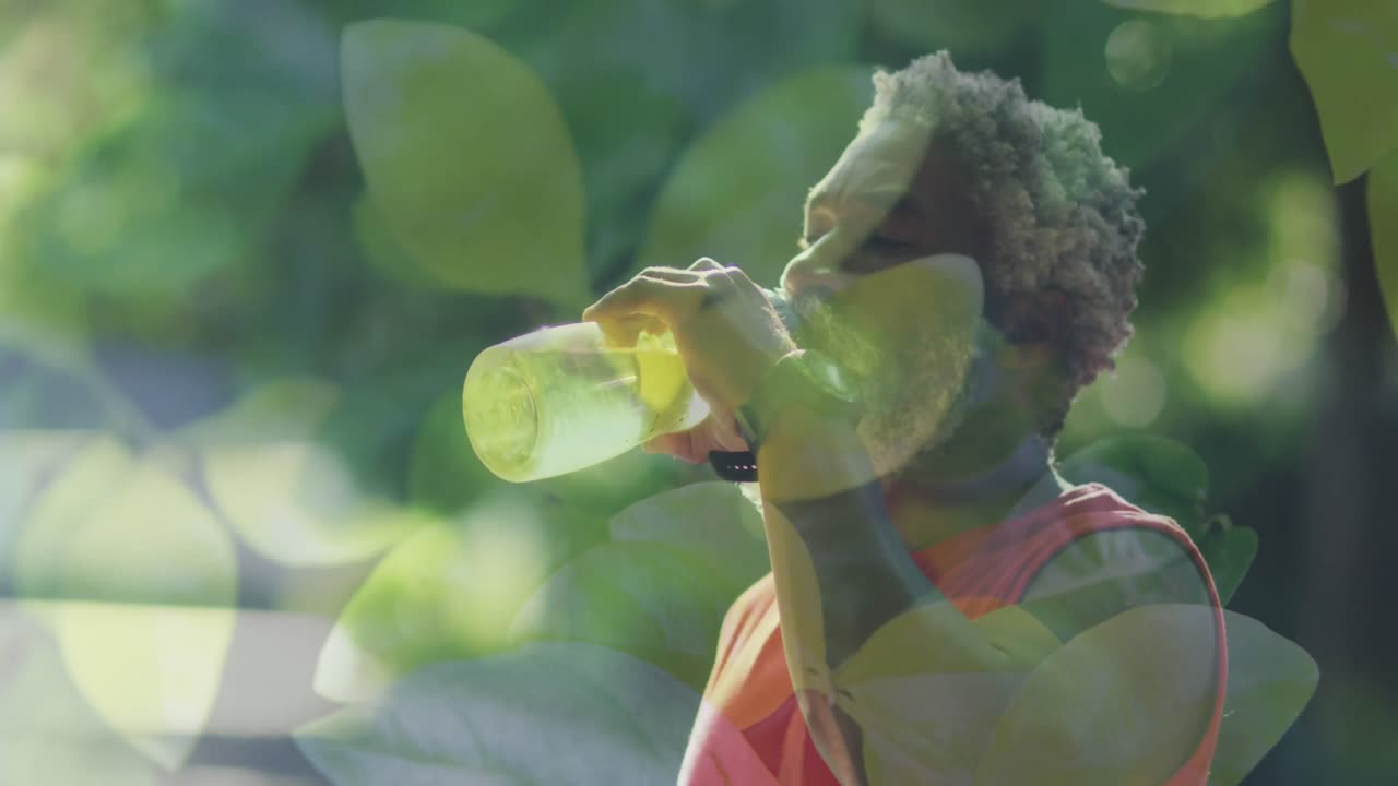 Animation of leaves over african american man drinking water, slow motion