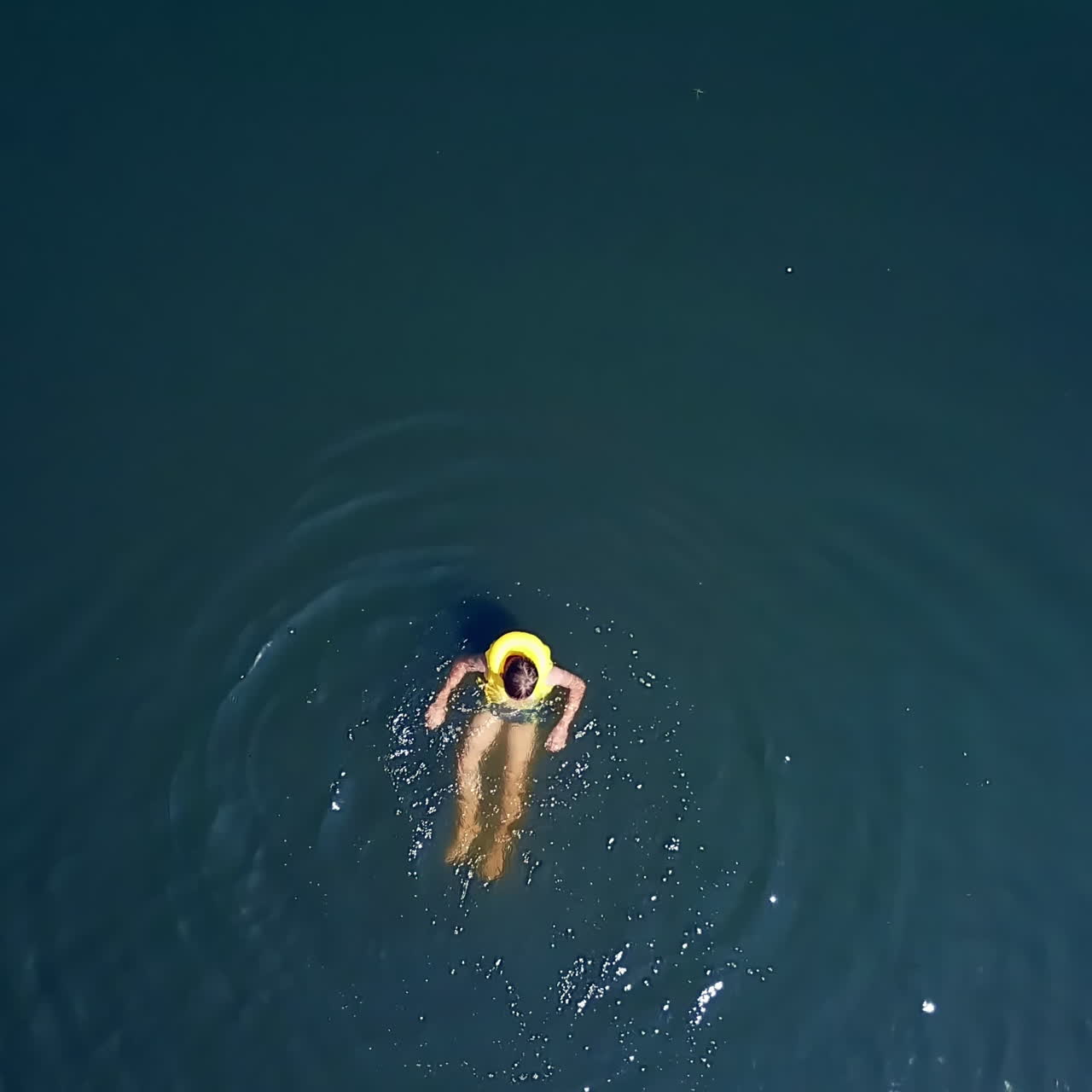 Aerial shot of a boy swimming in clear sea water. Top view of a boy swimming away camera in the middle of the ocean