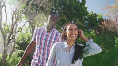 Video-De-Una-Feliz-Pareja-Diversa-Tomados-De-La-Mano-Y-Caminando-En-Un-Soleado-Jardín-Sonriendo