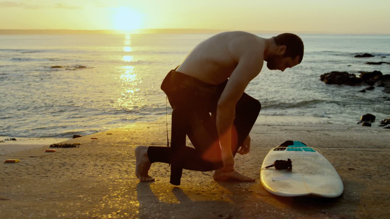 vista lateral de un hombre caucásico adulto con traje de surf en la playa durante la puesta de sol 4k