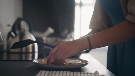 happy housewife is cooking breakfast for family lady in blue apron is frying pancakes closeup view