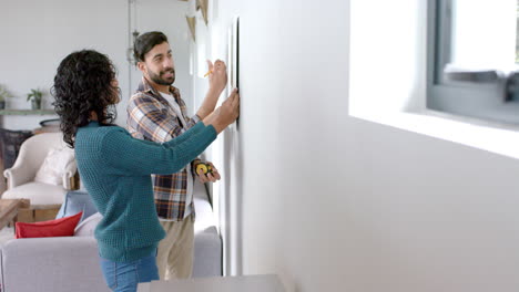 una feliz pareja biracial tomando medidas en la pared en casa, en cámara lenta