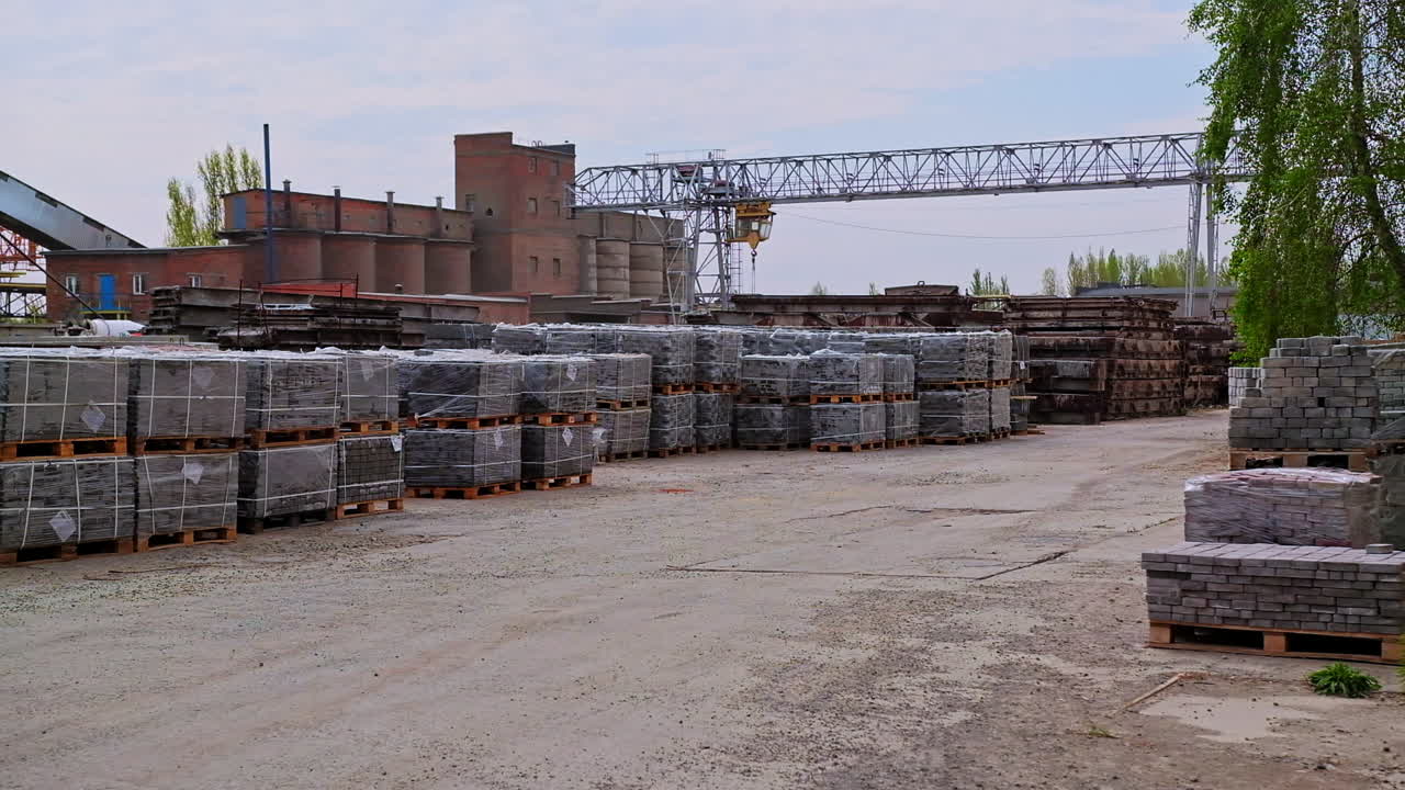 Industrial area with building materials stacked outside. Piles of grey bricks on wooden pallets at the backdrop of plant premises.