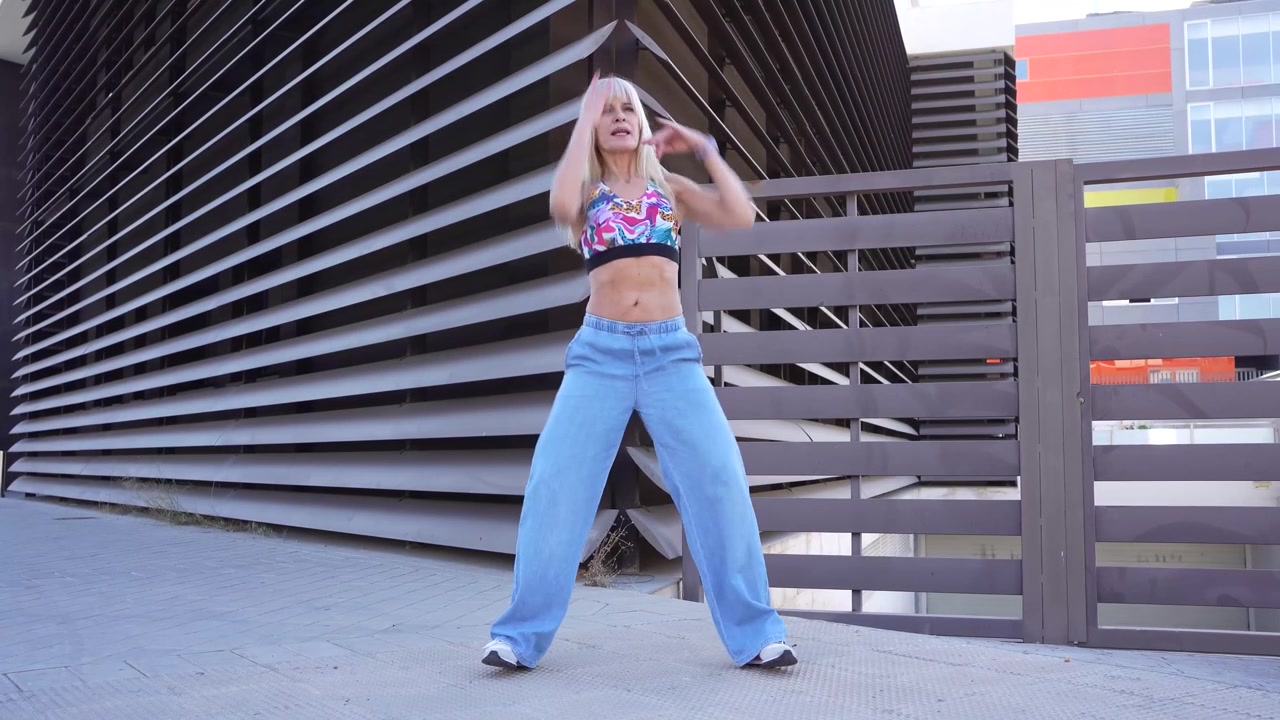 Donna bionda balla energicamente all'aperto, incarnando uno stile di vita attivo, in jeans e crop top.