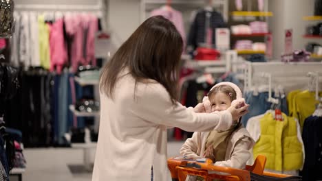 mother and daughter in a clothing store with girl in a shopping cart, put stylish headphones