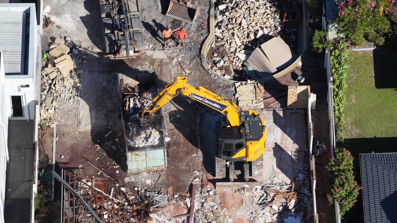 Vue Aérienne par Drone d'une Machinerie Jaune Déblayant des Débris dans un Conteneur sur un Terrain Résidentiel