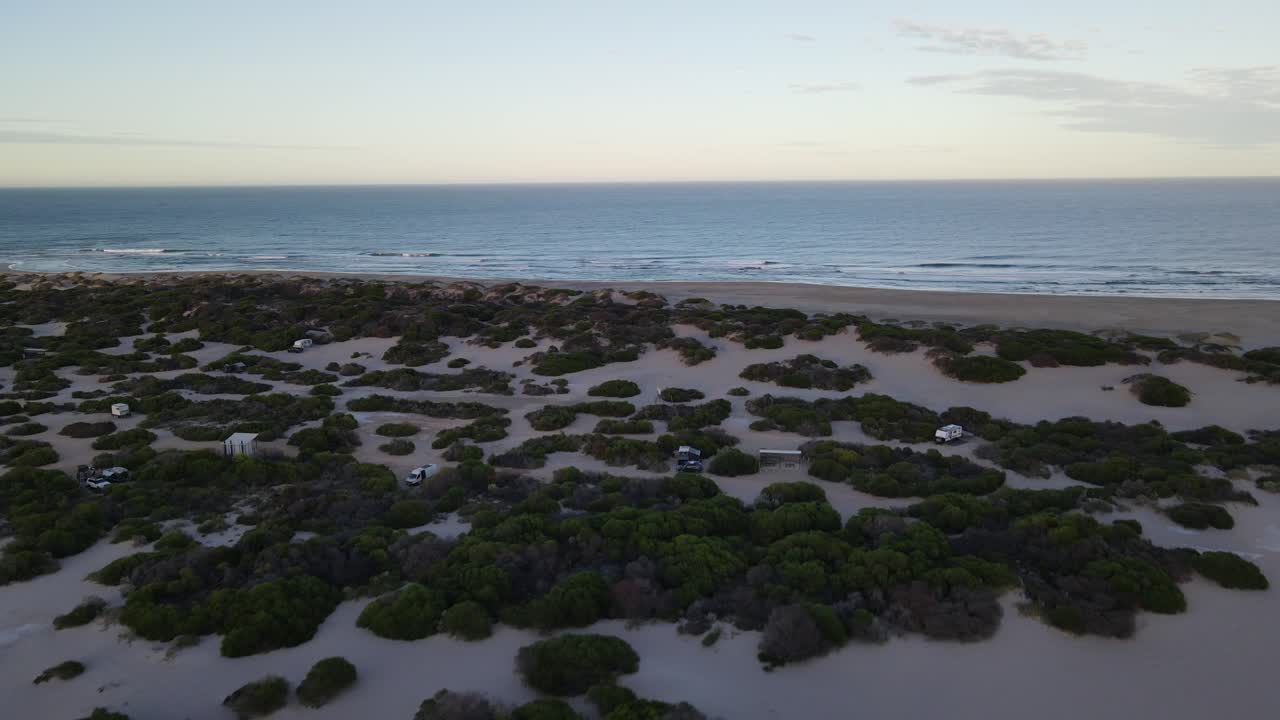 drone aéreo moviéndose desde un campamento junto a la playa a aguas prístinas durante el amanecer