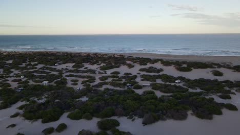 Drone-aerial-moving-up-from-a-beach-side-campground-to-pristine-water-during-sunrise