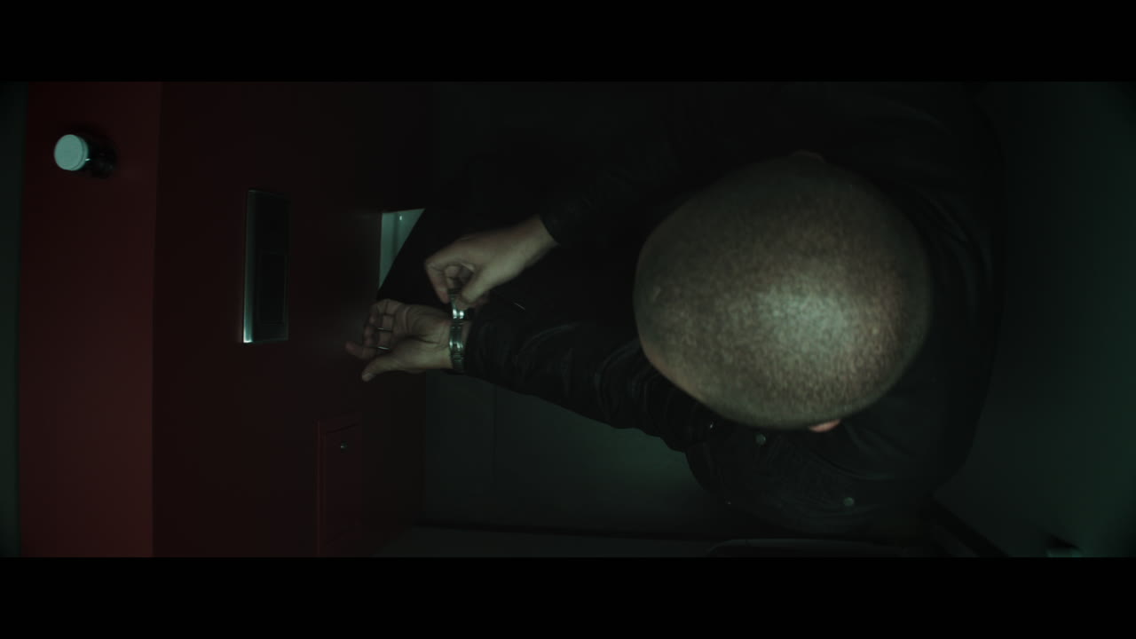 A bald dangerous looking man unpacks a black bag in the public toilet