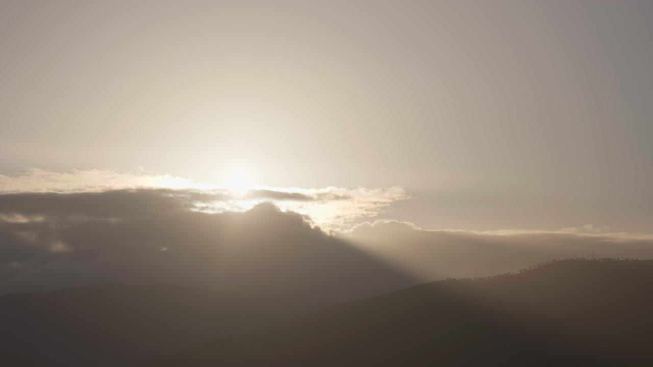 Dawn breaks with sunbeams piercing through dark clouds over a mountain range. Natural golden light