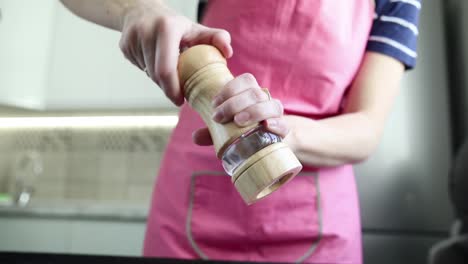 mujer usando un molinillo de pimienta en la cocina