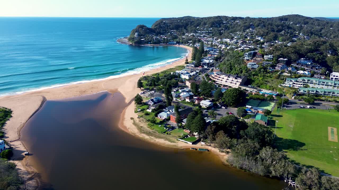 Drone aerial landscape of ocean waves breaking on Avoca Beach town with residential housing coastal lagoon coastline and bushland headland in Central Coast Australia travel tourism nature outdoors