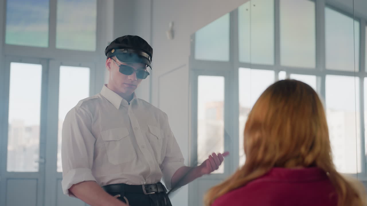 young boy wearing black cap and sunglasses taps baton on palm then slides it across head of seated girl as smoke drifts in background inside softly lit modern minimal studio with large windows