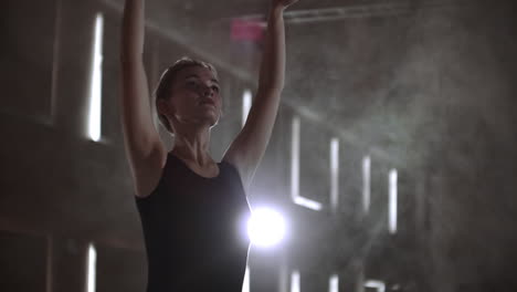 middle plan slow motion: a young ballerina girl performs graceful movements on the stage in a tutu and pointe shoes in the dark and smoke.