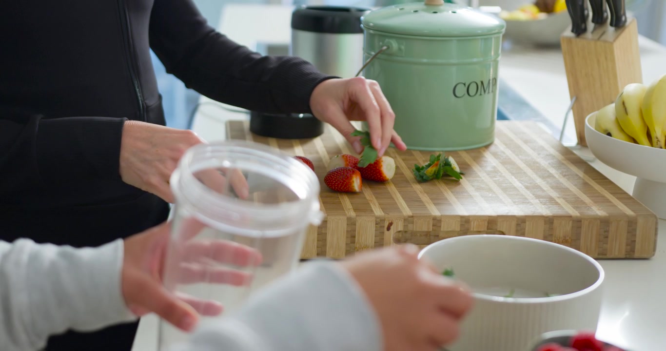 Due donne che preparano un frullato al bancone, aggiungendo frutti di bosco nel frullatore, tagliando frutta, con spazio per il testo.
