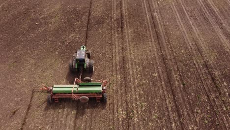 aerial follow shot of agricultural tractor plowing field with machinery during sunny day - tracking shot