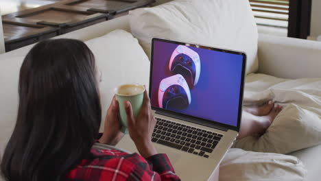 Biracial-woman-on-couch-with-coffee,-using-laptop-for-online-shopping,-slow-motion