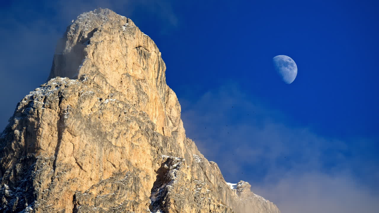 View of snow on the mountains in the Dolomites, Italy with the moon on the cloudy sky on the background