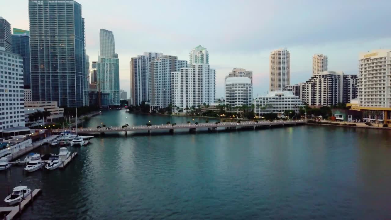 Aerial view rising over the sea, in the middle of high rise buildings, towards the Brickell key drive bridge, on a sunny morning, in Miami, Florida, USA - tilt down, drone shot