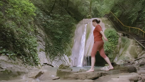 woman hiking by waterfall in a mountainous forest