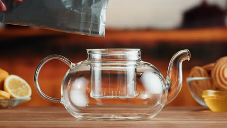 pouring loose leaf tea into a clear glass teapot