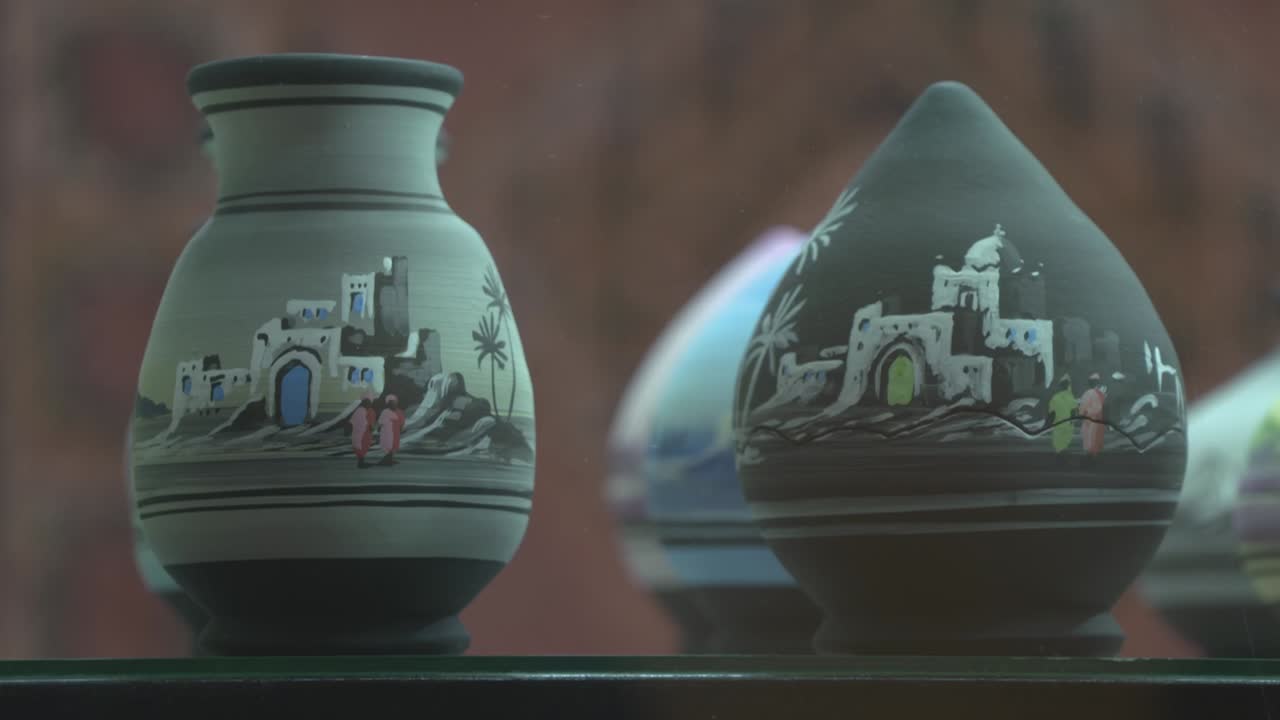 Vista dettagliata di oggetti di ceramica artigianale con architettura tradizionale marocchina dipinta a mano. I vasi presentano disegni in miniatura di edifici Kasbah bianchi, archi e palme