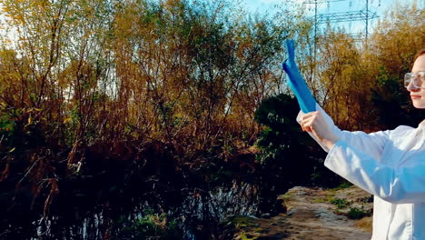 a young woman scientist at a creek, wearing protective eyewear and a lab coat