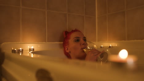 melancholy young woman drinking wine relaxing in a warm bath. close up shot.
