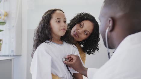 happy diverse doctor examining sick girl patient with stethoscope with her mother in slow motion