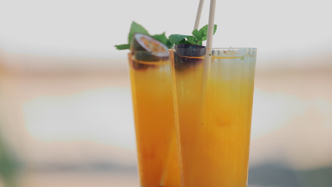 Two bright orange cocktails with mint and passion fruit on a small wooden table at a beach club