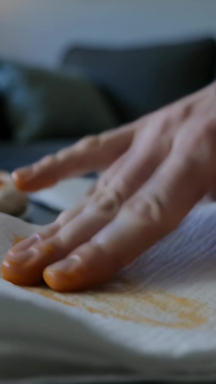 Vertical video: Seeing traces, pressing orange nails blotting paper towel by couch, lifting stain