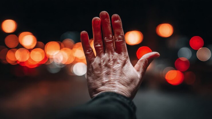 Una persona allunga una mano su uno sfondo di luci sfocate della città, evocando temi di connessione e umanità in un contesto urbano notturno