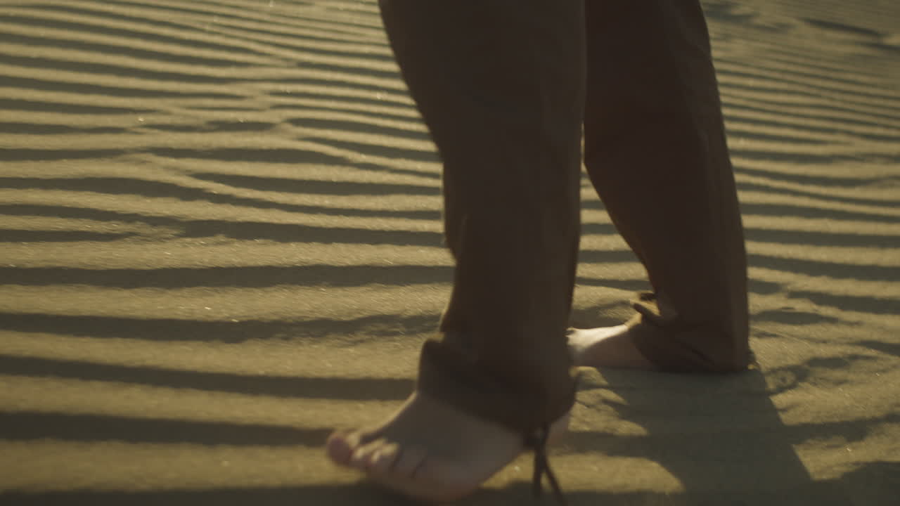 Persona a piedi nudi che cammina sulla splendida sabbia del deserto durante un tramonto