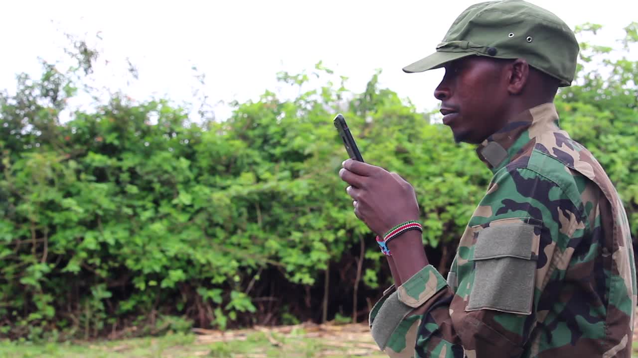 Militante guerrigliero africano che scrive messaggi al telefono, ripreso di profilo.